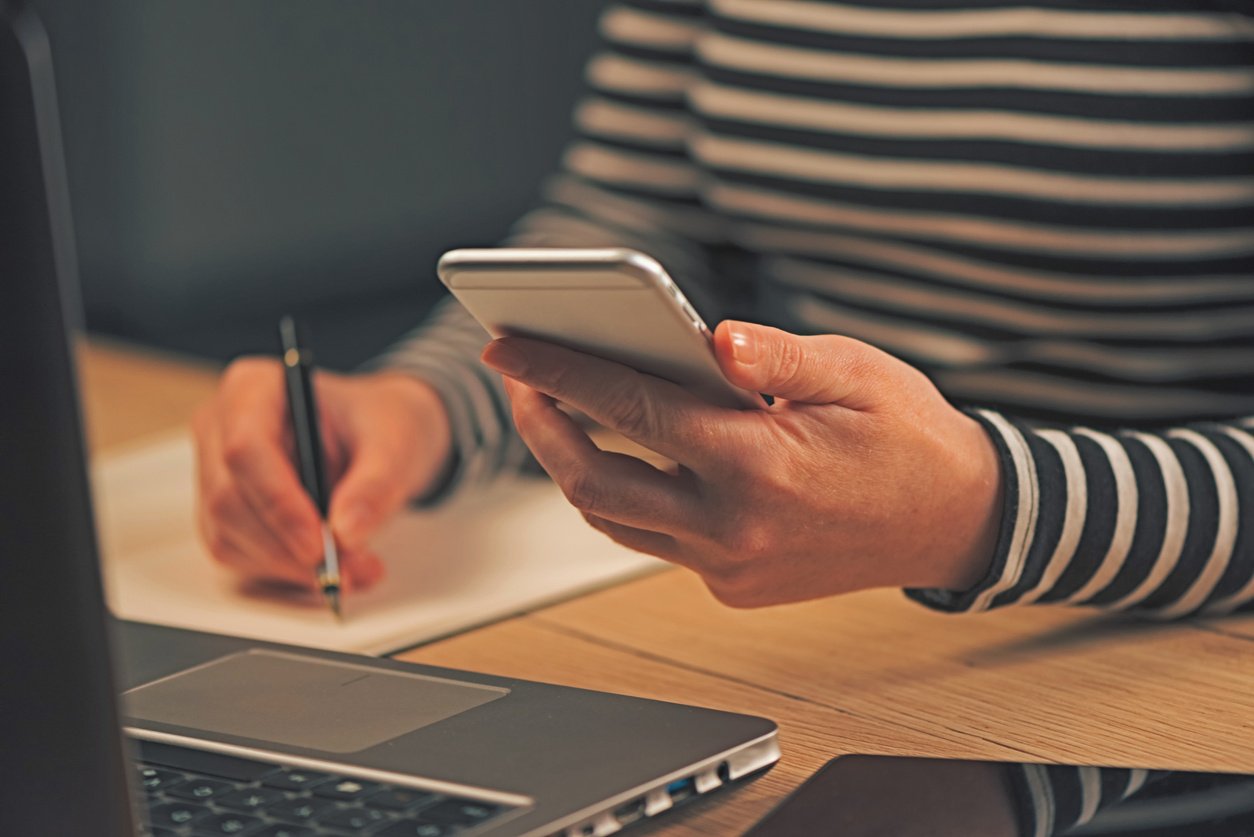 Woman Writing Contact List from Phone into Business Agenda